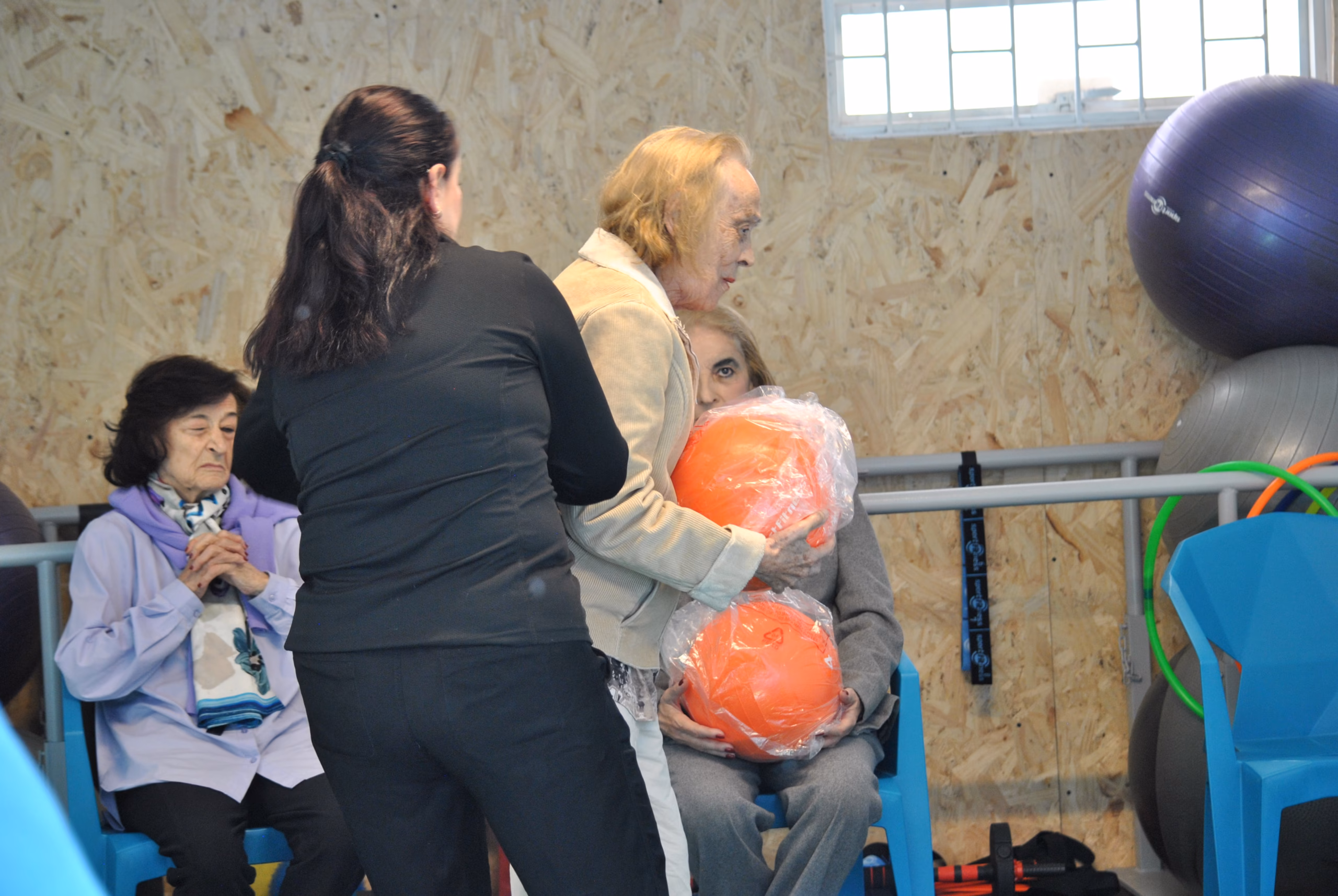Leidy García, directora del Club Tiempo y Vida, acompañando a una persona mayor en un ejercicio funcional con balón medicinal en el gimnasio