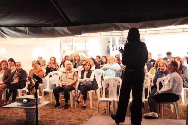 Facilitadora dando una charla de bienestar y envejecimiento activo a un grupo de adultos mayores bajo una carpa, en un programa para organizaciones del Club Tiempo y Vida